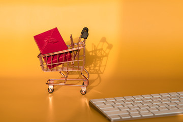 Shopping cart model and computer keyboard with gifts in front of yellow background