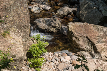 Fototapeta na wymiar stream flow through the rocky creek down the valley floor on a sunny day