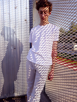 Portrait of a young guy of model appearance standing near a steel fence in the rays of the sun