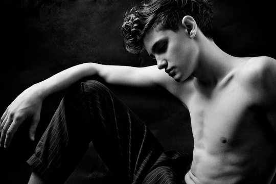 Black and white portrait of a young handsome guy with a naked torso in the studio against a dark background