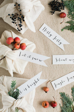 CHristmas greetings handwritten on tags close to gifts wrapped inside cotton napkins and decorated with botanical elements
