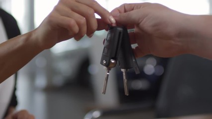 Close up shot of hands of female customer getting car key from salesman while buying new auto in dealership showroom