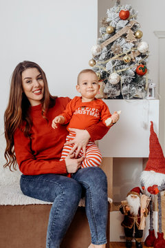 Young mother sitting on the sofa with her one year old son near Christmas tree