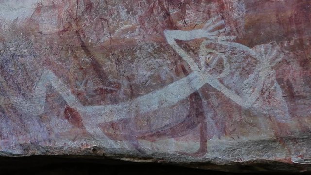 Close-up low angle still shot of an old white paint rock drawing of a man lying down on his back with hands spread above his head, historic scene