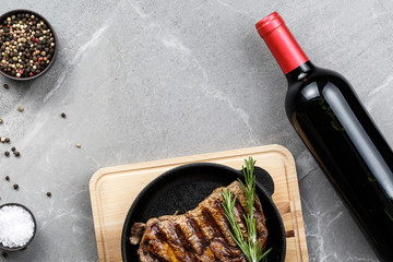 fried steak in pan with bottle of wine on gray marble table top view