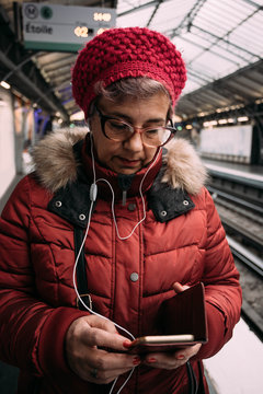 Woman standing on a subway station, waiting for metro and using a smart phone with headphone