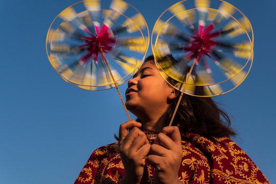 Teenage girl playing with pinwheels against sky