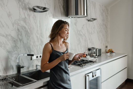Woman with coffee using phone in kitchen