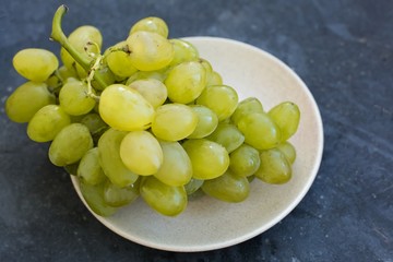 Ripe green grapes close-up on a plate, which stands on a blue concrete shabby background