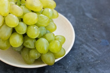Ripe green grapes close-up on a plate, which stands on a blue concrete shabby background