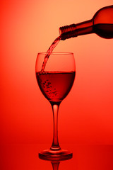 Pouring red wine into the wineglass close-up, isolated on pink gradient background