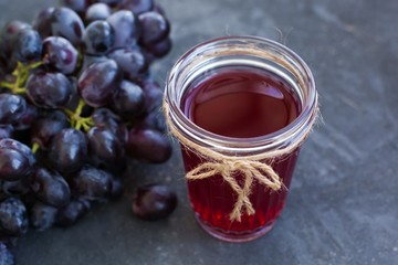 A bunch of ripe blue grapes and a glass of grape juice close-up on a blue shabby concrete background.