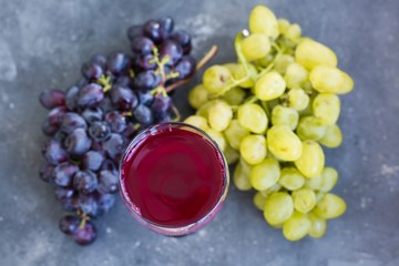 Bunches of ripe green and blue grapes and a glass of grape wine close-up on a blue shabby concrete...