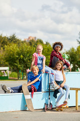 Fototapeta na wymiar Portrait of children smiling at camera while sitting on the bench and resting after riding on skateboards in the park