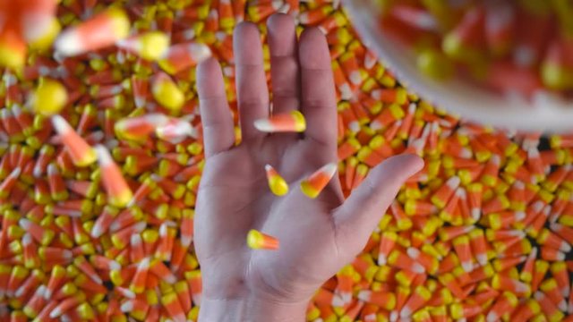 A large pile of Halloween candy corn is seen with a hand in view. Candy corn is seen dropping on top of the hand.
