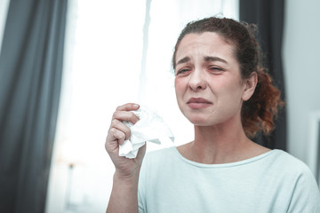 Curly woman holding napkin sneezing because of allergy