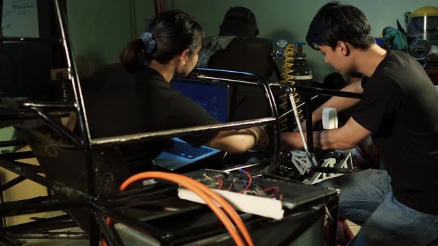 Asian engineer students are updating software with assembling and testing electric vehicles at the university. Concept of configuration, technological developments and renewable energy.
