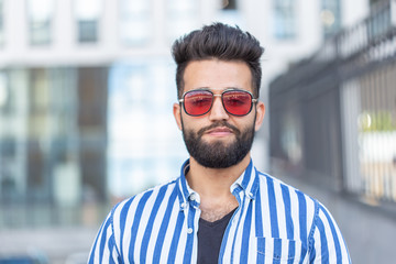 Portrait of cheerful positive stylish student guy in glasses with a mustache and beard outdoors. The concept of successful cheerful people.