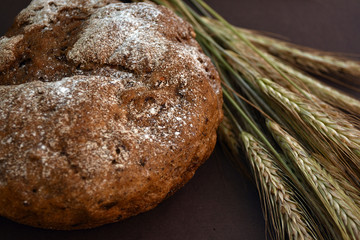 Loaf of bread and ears of wheat on a dark background. Closeup