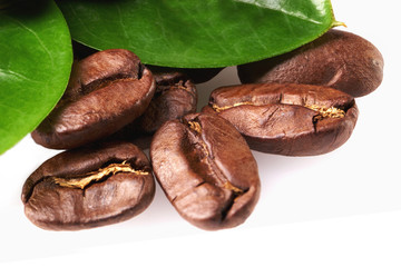 a handful of coffee beans with green leaves on a white background, isolate. concept: freshness of coffee beans. bunch of beans. close up