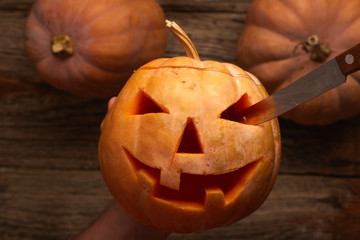halloween, decoration and holidays concept - close up of hands with knife carving pumpkin or jack-o-lantern at home