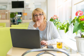 A woman with a laptop looks at a document in a cafe, office