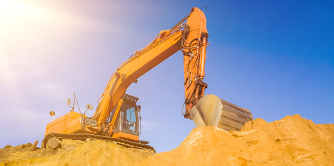 orange farbener Bagger auf der Baustelle Abbruch mit klarem blauem Himmel und Sonnenstrahlen