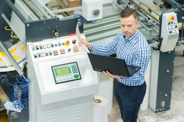 technician using laptop next to production line