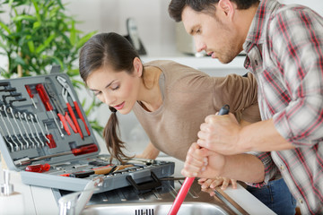 couple dealing with a blocked sink with a plunger © auremar