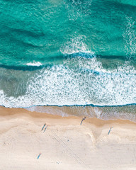 Antenne von Menschen, die bei Sonnenaufgang an einem Strand spazieren gehen, mit wunderschönem Sandstrand und sanften Wellen © FRPhotos
