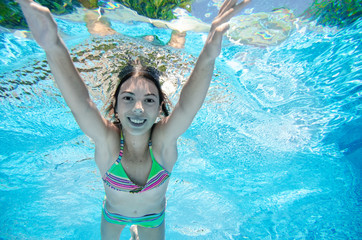 Child swims underwater in swimming pool, happy active teenager girl dives and has fun under water,...