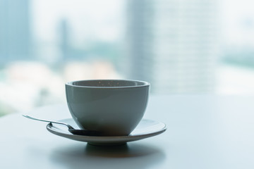 Coffee​ or tea​ cup​ blue color​ on the white​ table through the glass window of a tall building​ background, Business person's break time, Perspective of office lifestyle in big city.