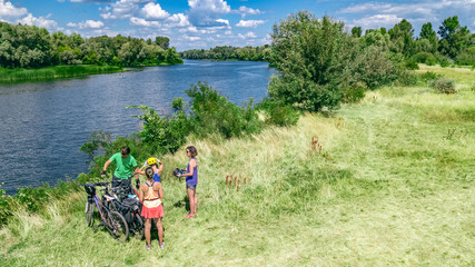 Fototapeta na wymiar Family on bikes cycling outdoors, active parents and kids on bicycles, aerial top view of happy family with children relaxing near beautiful river from above, weekend and vacation sport and fitness co