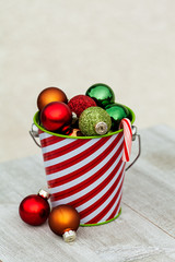Christmas striped bucket with festive balls on wooden table, season holiday concept