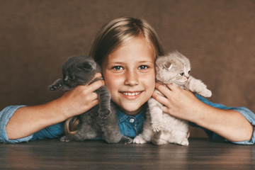 The child holds beautiful British kittens of different colors in the hands of
