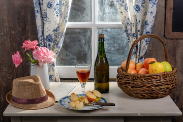 Bottle and glass of cider with apples. In rustic house