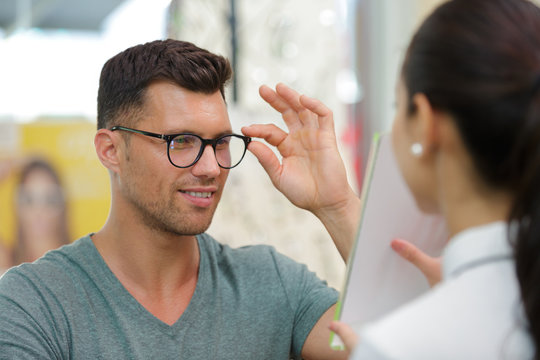 Man Trying On Eyeglasses And Looking In Mirror In Opticians