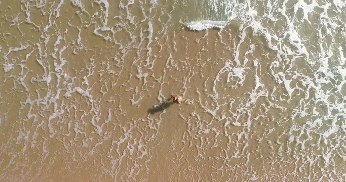 Dron encima de chica que anda por playa y olas