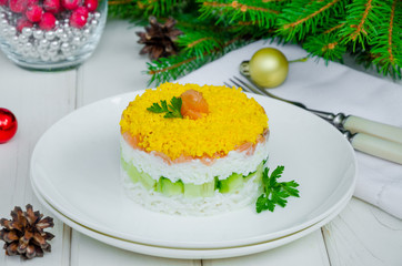 Salad with salted salmon (red fish), fresh cucumbers, rice and eggs on a white plate for Christmas and New Year.