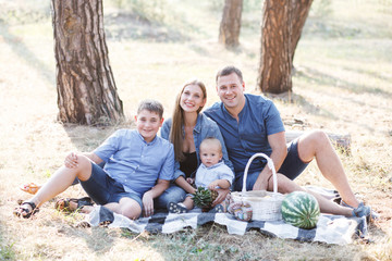 Beautiful happy family - parents and two sons, spend time in nature, laughing, eating fresh fruits and enjoying life