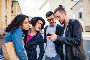 A group of young friends standing outdoor in town, using smartpone.