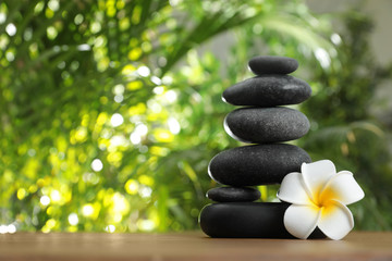 Table with stack of stones, flower and blurred green leaves on background, space for text. Zen concept