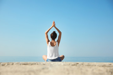 Fototapeta na wymiar Beautiful young woman practicing yoga near sea