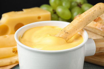 Pot of tasty cheese fondue and bread stick on table, closeup