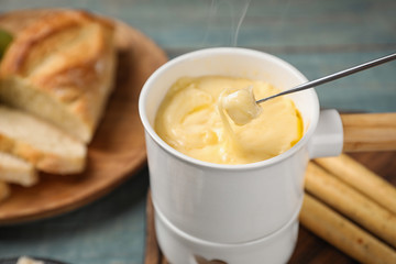 Pot of tasty cheese fondue and fork with bread on blue wooden table