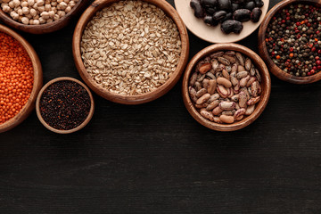 top view of raw beans, cereals and spice in bowls on dark wooden surface with copy space