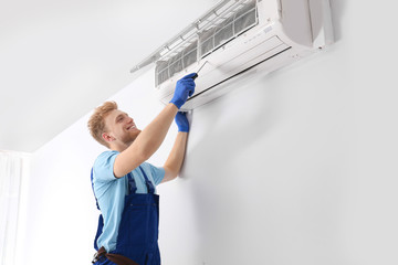 Professional technician maintaining modern air conditioner indoors