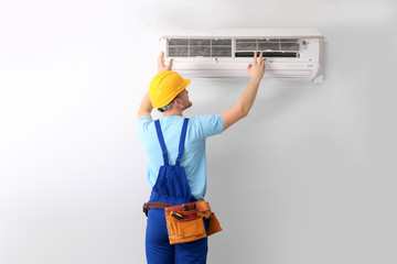 Professional technician maintaining modern air conditioner indoors