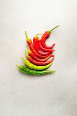 Hot spicy green and red pepper on a grey stone background .