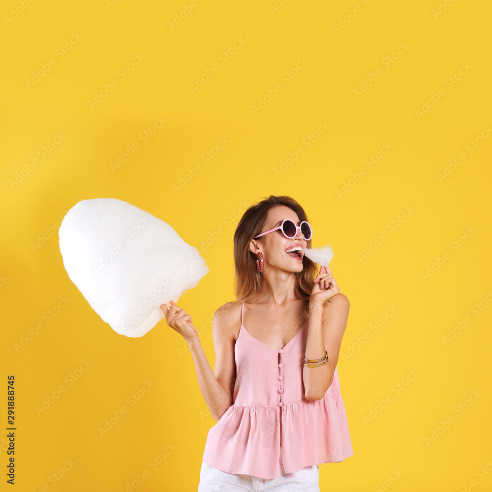 Wall mural Happy young woman eating cotton candy on yellow background